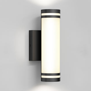 The Artika Bradley modern LED indoor-outdoor wall light 3 CCT features a black cylindrical frame with a frosted white diffuser, mounted on a light gray wall, emitting light both upward and downward.