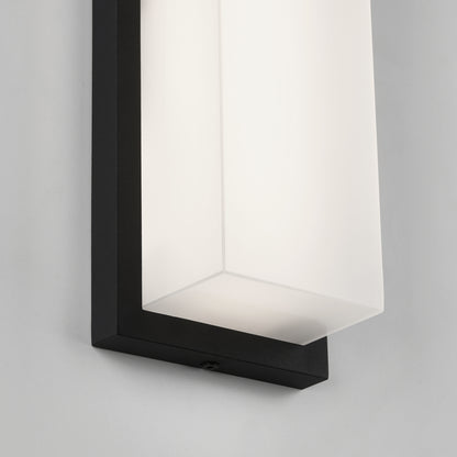 A close-up of a modern wall light fixture with a rectangular black frame and a frosted white glass shade, mounted on a white wall.