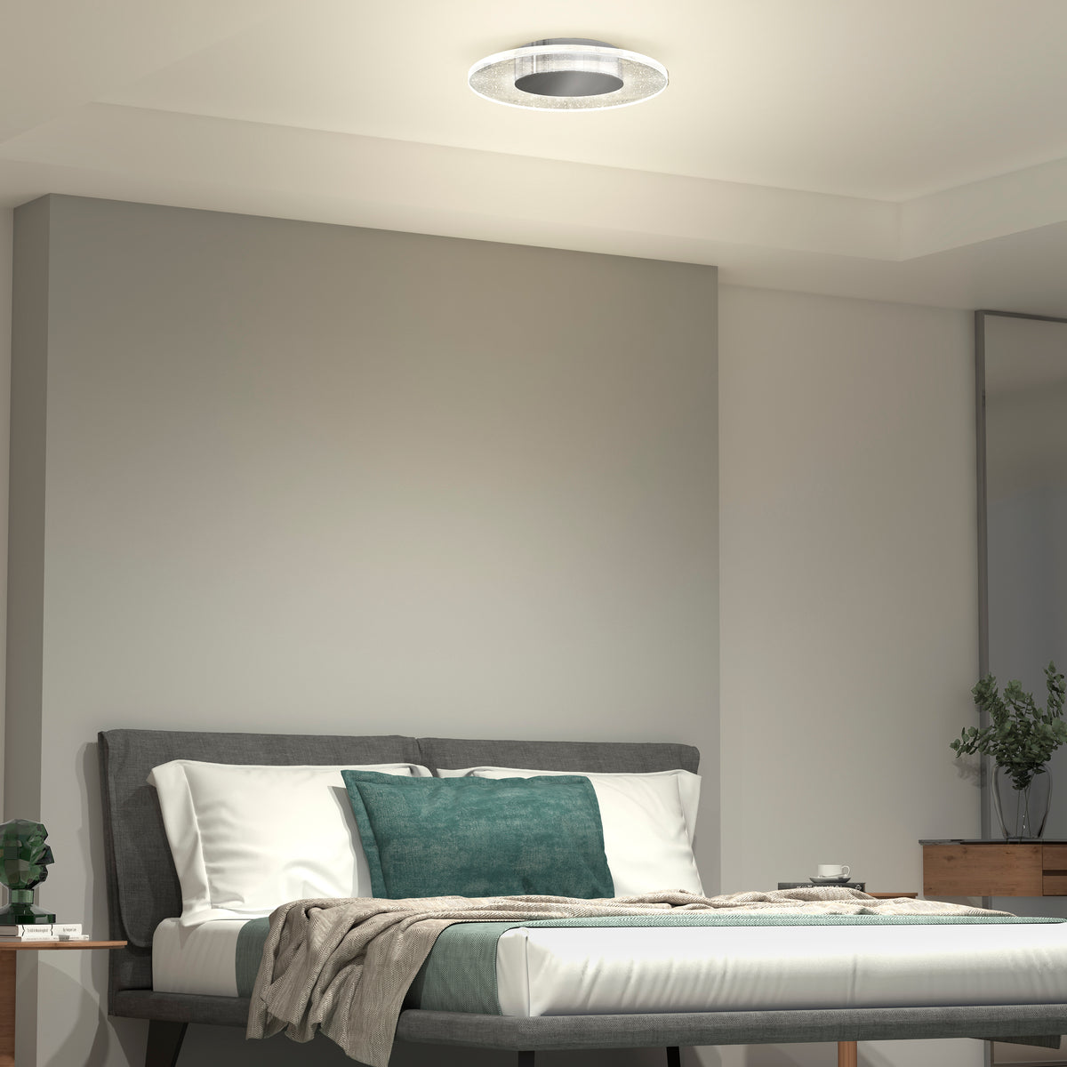 A modern bedroom features a neatly made bed with teal and white pillows, minimalistic decor, and a dresser with a plant. The room is illuminated by the Artika Essence Disk LED flush mount ceiling light.