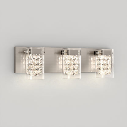 A modern wall-mounted light fixture with three rectangular lights, each featuring a crystal-like design and glass covers, set on a brushed metal backplate against a light gray wall.