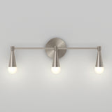 A modern wall-mounted light fixture with three brushed metal cone-shaped holders, each supporting a round white bulb, set against a plain light gray wall.