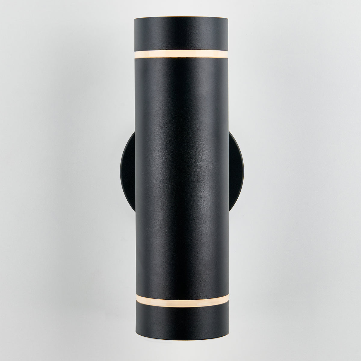 A modern, cylindrical black wall sconce with thin horizontal light bands near the top and bottom, mounted on a light gray wall.