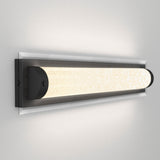 A modern wall-mounted light fixture with a rectangular black frame and a glowing cylindrical frosted glass shade, casting soft, even light on a white wall.