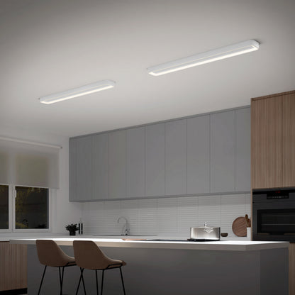 Modern kitchen with gray cabinets, wood accents, white countertop island, two beige barstools, and the Artika Aiden 48 in. LED modern flush mount light 5 CCT. Features include an oven, sink, window with white blind, and sleek rectangular fixtures.