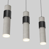 Three modern cylindrical pendant lights with a concrete texture and black metal accents hang against a plain gray background. The lights are illuminated, emitting a soft white glow.