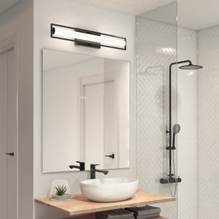Modern bathroom with a round white vessel sink on wood countertop, large mirror, Artika Rialto modern LED bathroom vanity light 3 CCT (dimmable), black faucet, folded towels, potted plant, and glass-enclosed shower with rain showerhead.