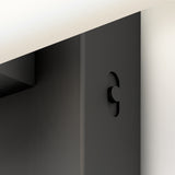 Close-up of a black metal object with a circular button or knob on its surface, partially obscured by a light-colored flat panel above it. The design appears minimalistic and modern.