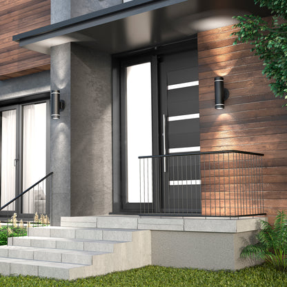 Modern house entrance featuring a black front door with horizontal glass panels, concrete steps, metal railing, and Artikas C7 indoor-outdoor wall lights. Exterior includes wood and concrete finishes, green grass, and a small tree.