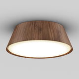 A modern ceiling light fixture with a cylindrical, wood-textured outer casing and a glowing, round white diffuser, mounted against a plain gray ceiling.