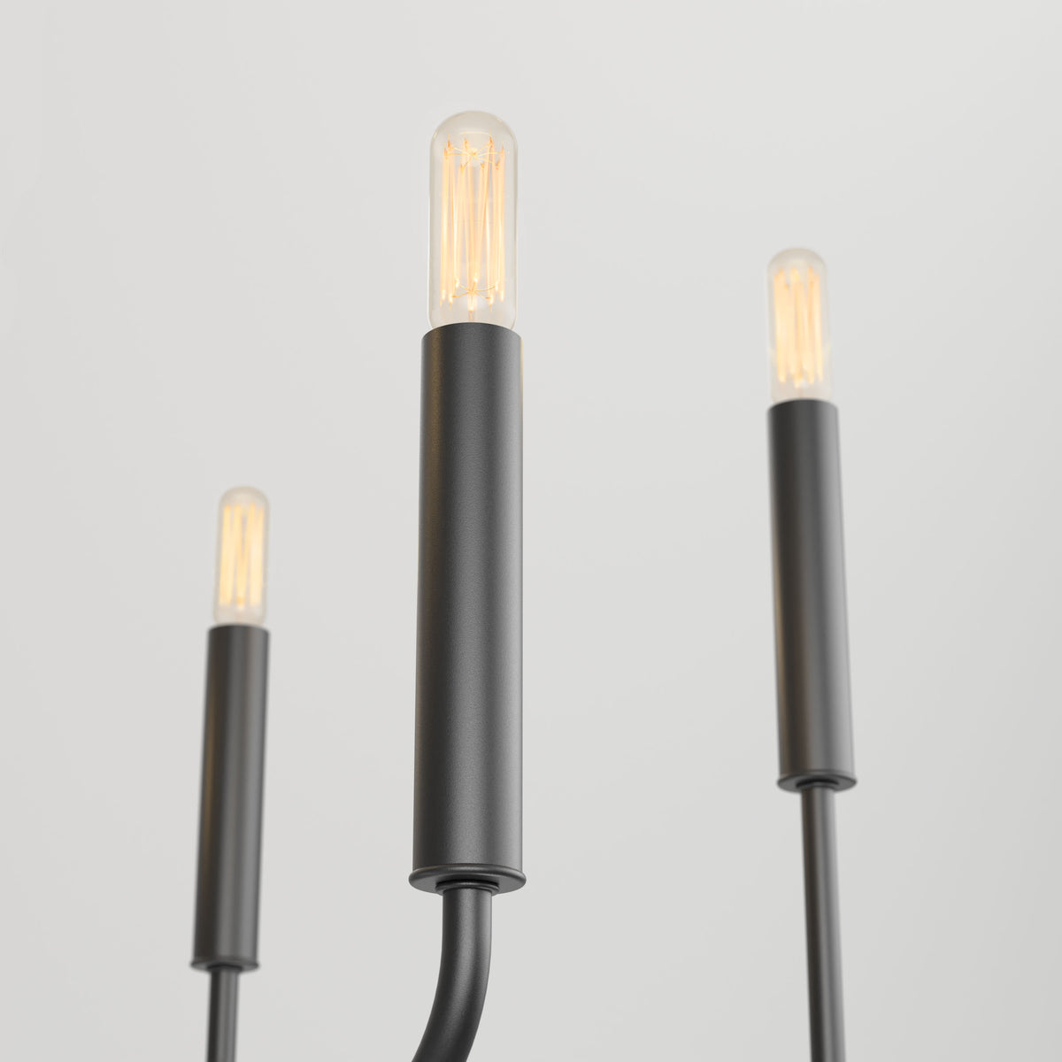The Artika Manchester 6-light pendant features three modern black cylindrical fixtures with exposed filament bulbs, standing upright on a plain white background. The central fixture is in focus, while the others are slightly blurred.