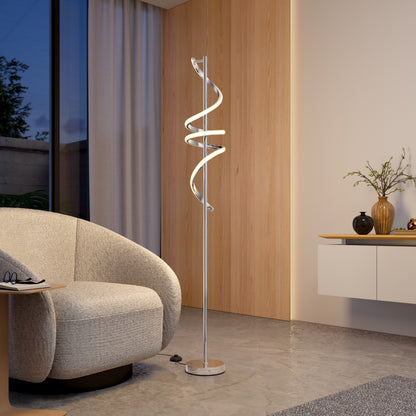 A modern living room featuring a textured gray armchair, the Artika Coda modern LED floor lamp 5CCT with a twisted design, a wooden accent wall, floating sideboard, and a vase with branches by a large window with sheer curtains.