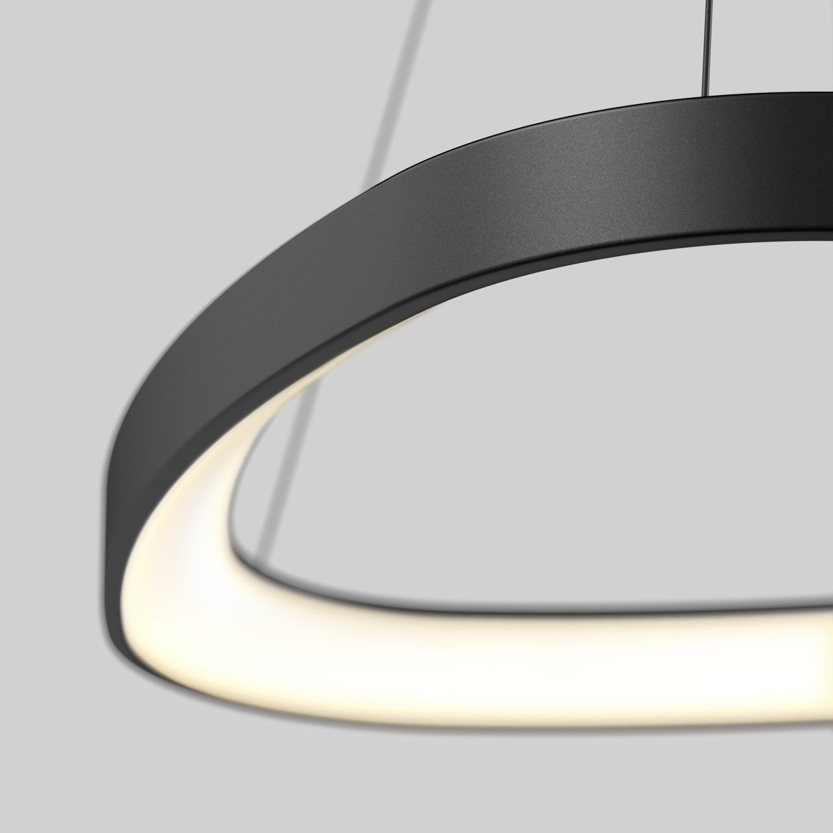 A close-up of a modern, black, oval-shaped pendant light with a glowing white interior, suspended by two thin wires against a plain grey background.