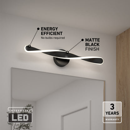 The Artika Finley LED modern bathroom vanity light 3 CCT, in matte black, is mounted above a mirror. Labels highlight energy efficiency, integrated LED (no bulbs needed), and a 3-year warranty, with wood panel and neutral walls in the background.