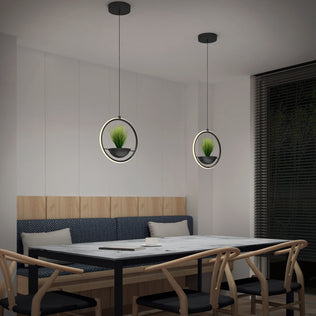 Modern dining area with a marble table, wooden chairs, and two Artika Colin LED modern planter pendant lights (5 CCT) hanging above the table. Each pendant features a small potted plant. A window with blinds is on the right.