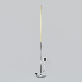 The Artika Arc LED Floor Lamp features a minimalistic, modern design with a slim vertical light on a round base, plugged into a wall outlet and set against a plain light gray background.