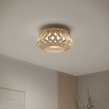 A ceiling light fixture with a woven, lattice-like wooden shade emits soft, warm light. The ceiling and upper corner of a modern, minimalist room with neutral colors are visible.