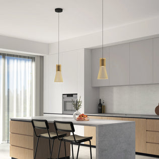Modern kitchen featuring light wood cabinets, a gray island with two black chairs, and two Artika Kiyo modern LED pendant 3 CCT lights. Large window with sheer curtains brings in natural light. Fruit bowl and vase on the island enhance the minimalist look.