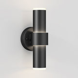 A modern, cylindrical black wall sconce with lights on both ends is mounted on a light gray wall, emitting soft illumination upwards and downwards.
