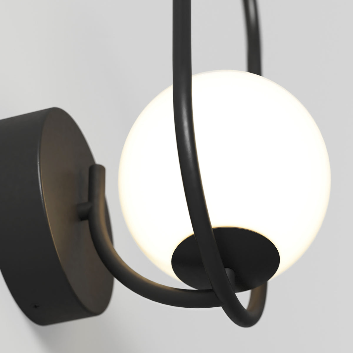 A modern wall-mounted light fixture with a round, white frosted glass globe and black metal frame, photographed against a plain light-colored wall.