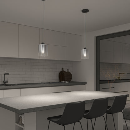 Modern kitchen with gray countertops, three black chairs at an island, white cabinetry, subway tile backsplash, and two Artika Haze glass pendant lights above the island. A black faucet and cutting boards sit on the counter.