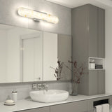 Modern bathroom with a large mirror, oval sink, wall-mounted faucet, and grey cabinets. A light fixture above the mirror illuminates the space, and a vase with branches decorates the countertop.