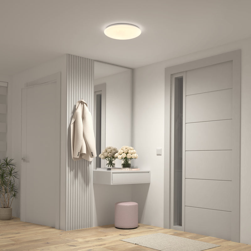 A modern hallway with white walls, a coat, flowers, a pink stool, and the Artika Empress 13" LED ceiling light with 3 CCT.