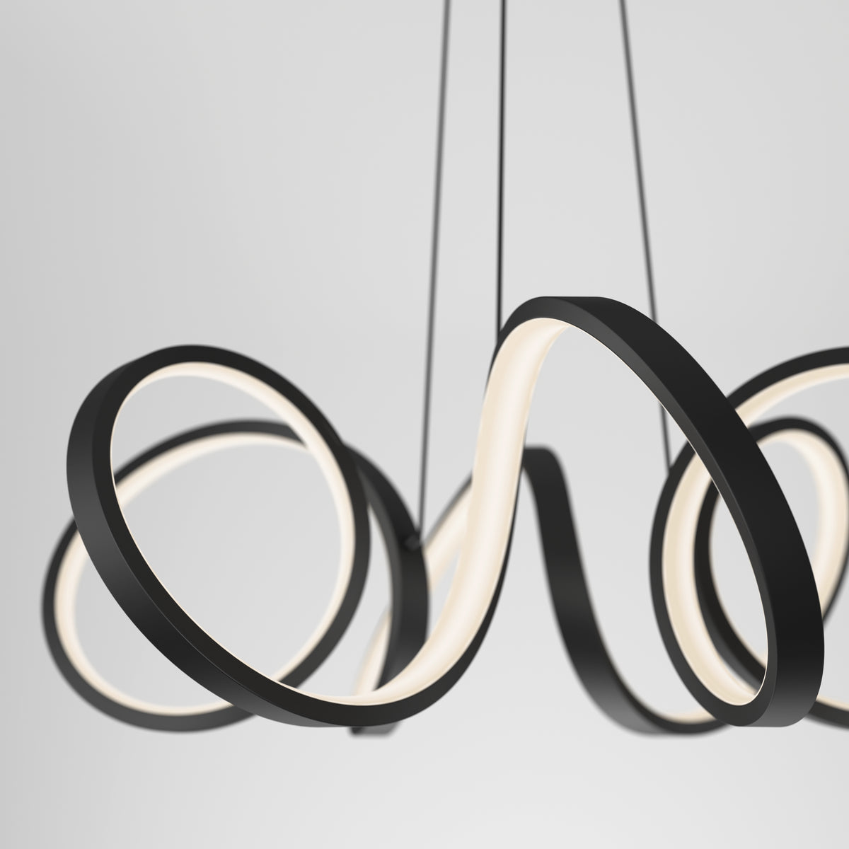 Close-up of the Artika Swirl Ribbon LED pendant light, featuring black wavy loops and integrated white LEDs, suspended by thin black cables against a light gray background.