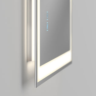 The Artika Sofia LED mirror 3 CCT with defogger features a sleek, minimalist design, touch-sensitive blue icons, and a white illuminated border. Mounted on a light gray wall, this modern mirror offers adjustable lighting for any space.