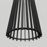 Close-up view of a modern, black, cylindrical lampshade made of vertical metal rods arranged in a circular pattern, photographed against a plain light gray background.
