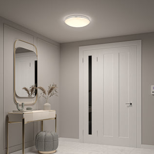 A modern entryway with light gray walls, a white door, a console table with a mirror, decorative vases, a round ottoman, marble flooring, and the Artika Sparkle 15 in. LED modern flush mount light (5 CCT) on the ceiling.