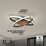 Modern ceiling light fixture with overlapping LED rings, black and walnut wood finish, labeled energy efficient and 5 years warranty in a bright living room. Text indicates integrated LED and no bulbs required.