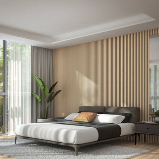 Modern bedroom featuring a low bed, gray bedding, patterned cushion, large window with sheer curtains, indoor plant, gray rug, bedside table, and Artika Sonofold sound-absorbing wall panel kit as a vertical accent under natural light.