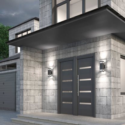 Modern house entrance with double gray doors and horizontal glass panels, flanked by Artika Strike indoor-outdoor wall lights. Light gray stone tiles cover the exterior, topped with a large overhang above the entryway.