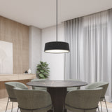 A modern dining area with a round black marble table, four green velvet chairs, a black pendant light, a potted plant, floor-to-ceiling curtains, and wood paneling on the wall.