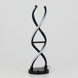 A modern table lamp with two intertwined black and white LED light strips, resembling a DNA double helix, stands on a round black base against a plain white background.