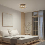 A modern, minimalist bedroom with a low wooden bed, white bedding, a gray throw, a simple nightstand, a large window with sheer curtains, a decorative branch in a vase, and a geometric ceiling light.