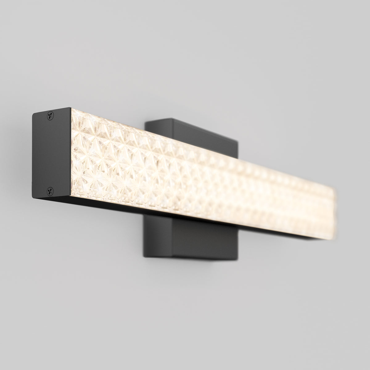 A modern wall-mounted light fixture with a rectangular black base and a long, textured, illuminated glass panel, set against a plain light gray wall.