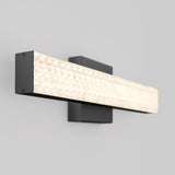 A modern wall-mounted light fixture with a rectangular black base and a long, textured, illuminated glass panel, set against a plain light gray wall.