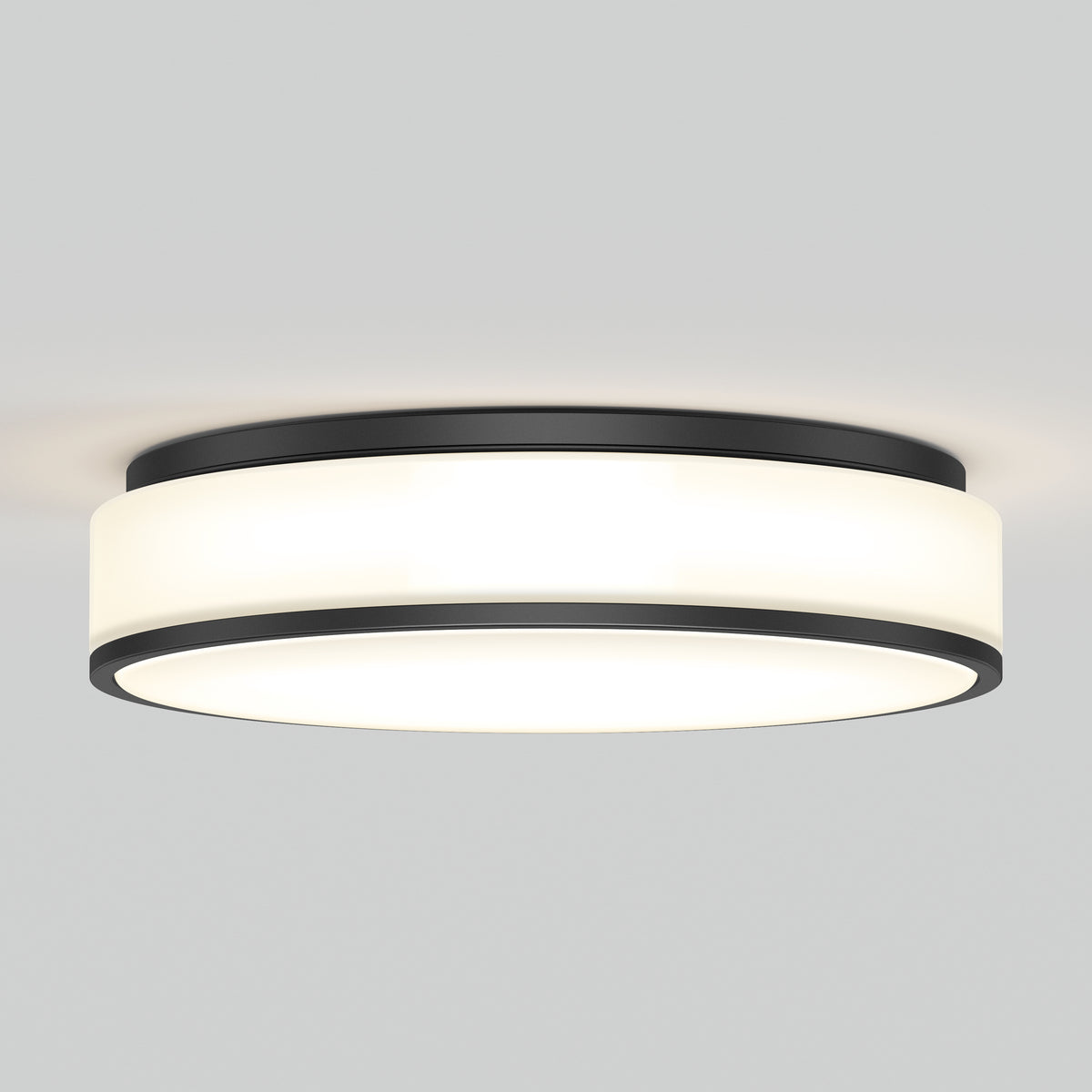A modern, round, flush-mount ceiling light with a black metal frame and a white frosted diffuser, emitting a soft, even glow against a plain light gray ceiling.