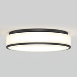 A modern, round, flush-mount ceiling light with a black metal frame and a white frosted diffuser, emitting a soft, even glow against a plain light gray ceiling.