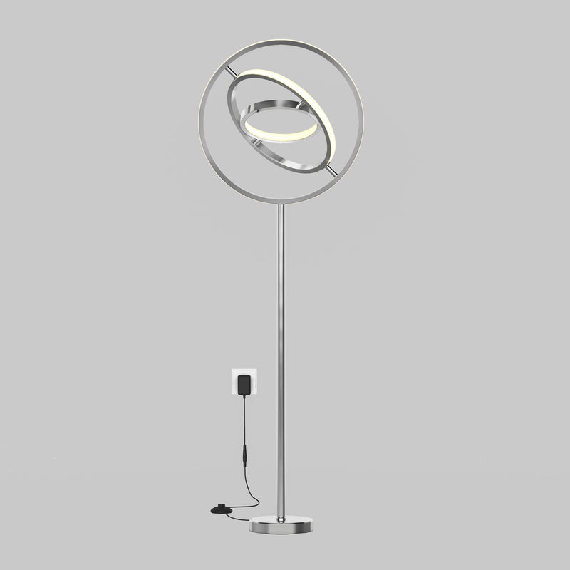 The Artika Pivot modern LED floor lamp 3 CCT features a sleek silver finish, circular elements, and an illuminated ring, shown plugged into a wall socket against a plain gray background.
