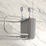 A grey toothbrush holder with two toothbrushes, one blue and one purple, sits on a metal bathroom shelf mounted against a white marble-tiled wall.