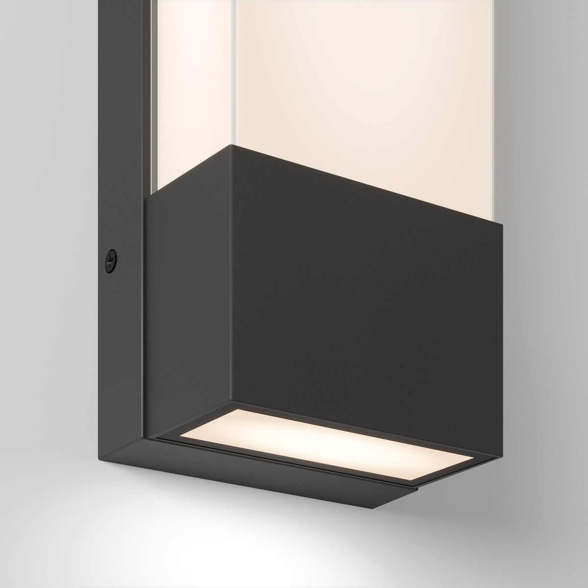 Close-up of a modern wall-mounted light fixture with a rectangular black metal base and frosted glass, emitting a soft white light downward and through the top section.