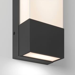 Close-up of the Dixon indoor-outdoor LED wall light by Artika, featuring a rectangular black metal base and frosted glass, casting a soft white glow downward on a light gray wall.