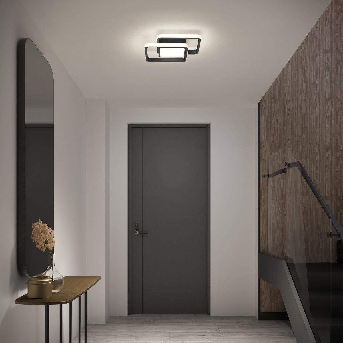 A modern hallway features an Artika Romeson 11 in. LED flush mount light, a dark door, a console with a vase of beige flowers on the left, large mirror above, and glass-railed stairs on the right.