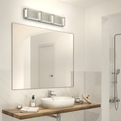 Modern bathroom featuring an Artika Subway Essence 3 LED vanity light above a large mirror, with a wooden sink counter, rectangular vessel sink, soap dispenser, and white tiled walls. A shower appears in the background.