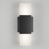 A modern wall sconce with a rectangular black center panel and frosted white diffusers on the top and bottom, emitting soft light upward and downward against a neutral background.