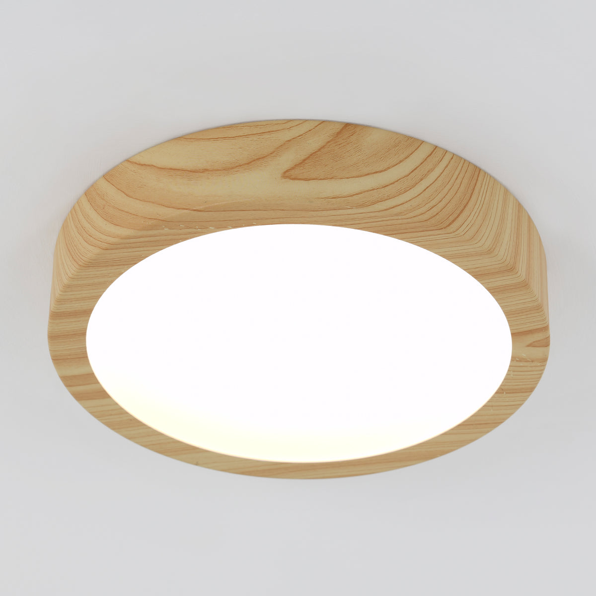 A round ceiling light with a smooth, light wood frame and a bright white diffuser, mounted on a white ceiling.