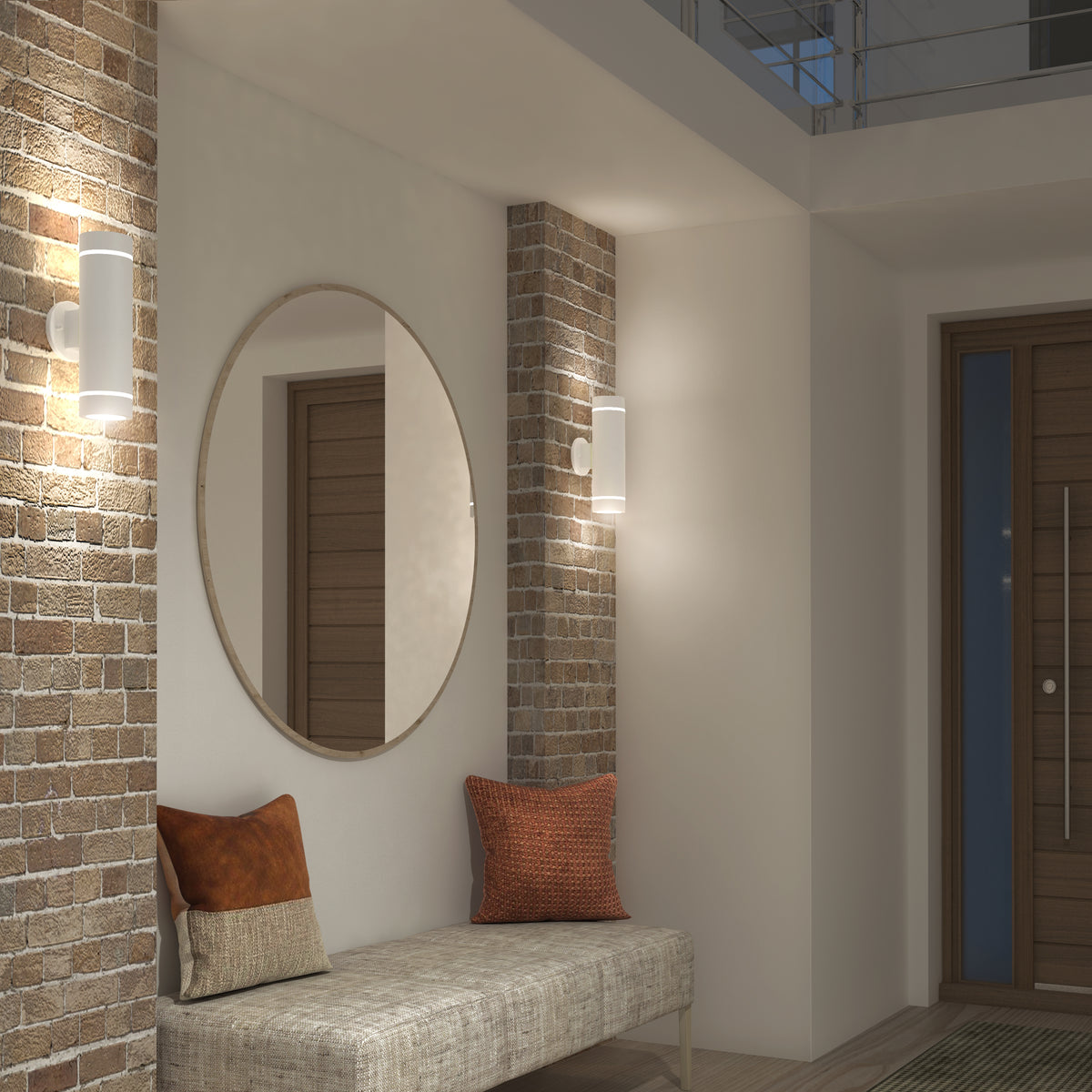 A modern entryway with exposed brick columns, a round mirror, wall sconces, a cushioned bench, two accent pillows, and a wooden door in the background. Warm lighting creates a cozy atmosphere.
