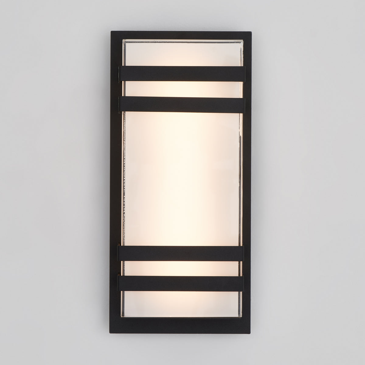 The Artika Glowbox 3 indoor-outdoor LED wall light features a rectangular design with frosted glass, a black metal frame, and two horizontal black bars. It emits a soft glow through the center glass panel.